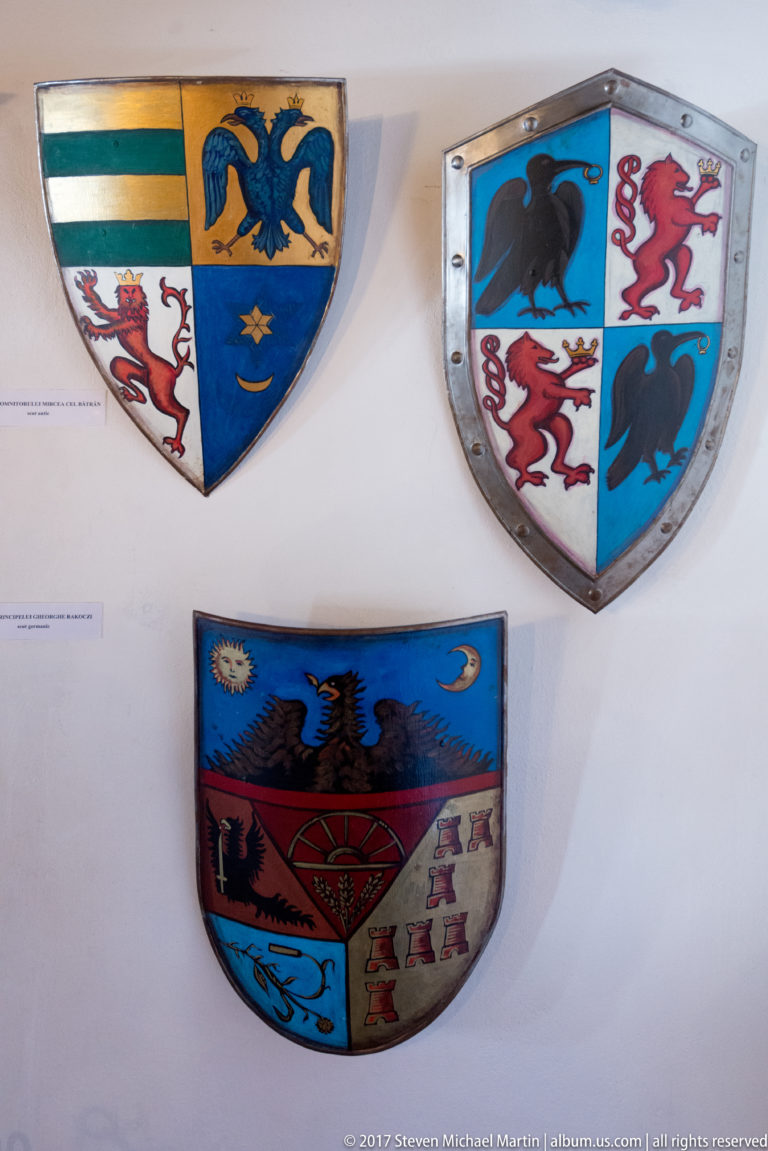Three painted heraldic shields with eagles, stars, lions, and multicolored quartered fields.