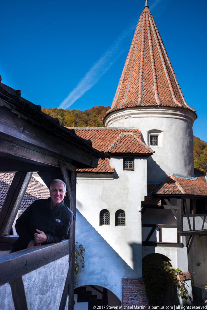 Round white tower with conical tile roof beside timber gallery, with a visitor leaning on the railing.