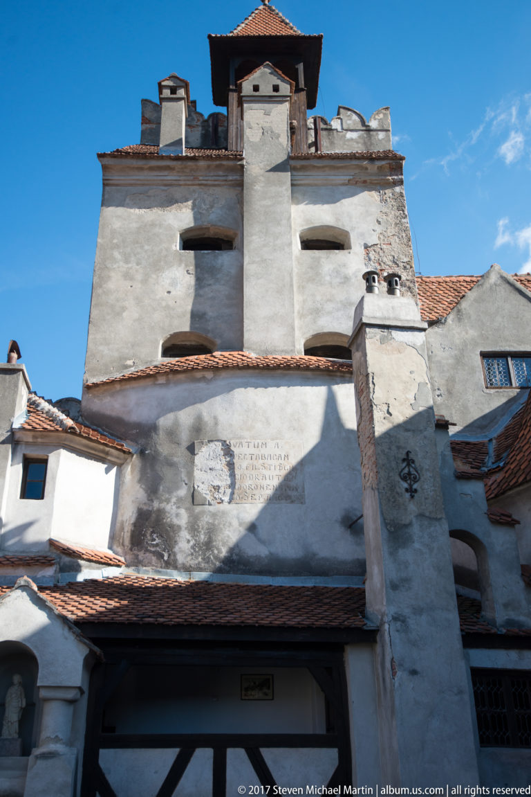 Tall white castle tower rising above layered red-tiled roofs, chimneys, and weathered courtyard walls.