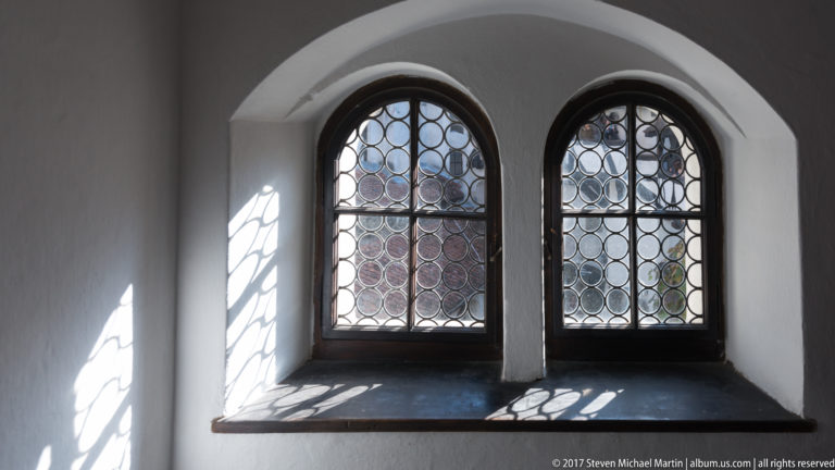 Two arched windows with circular leaded glazing set in a deep white recess, casting patterned shadows.