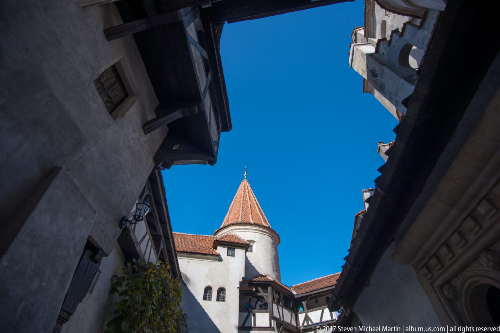Conical red-tiled turret seen from below between dark eaves and walls in Bran Castle’s courtyard.