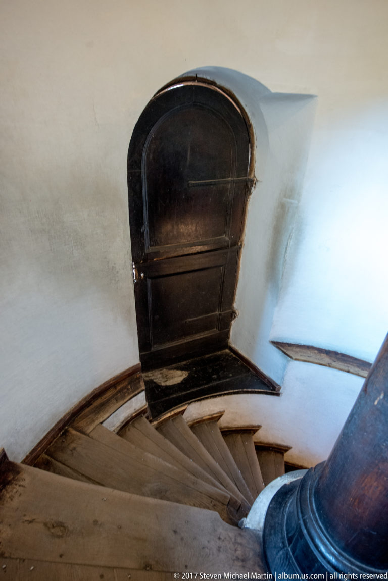 Curved wooden staircase with wedge-shaped treads and dark rounded doorway inside Bran Castle.