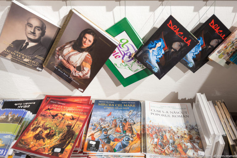 Gift-shop display of Romanian history books and Dracula-themed titles arranged on shelves and hanging supports.