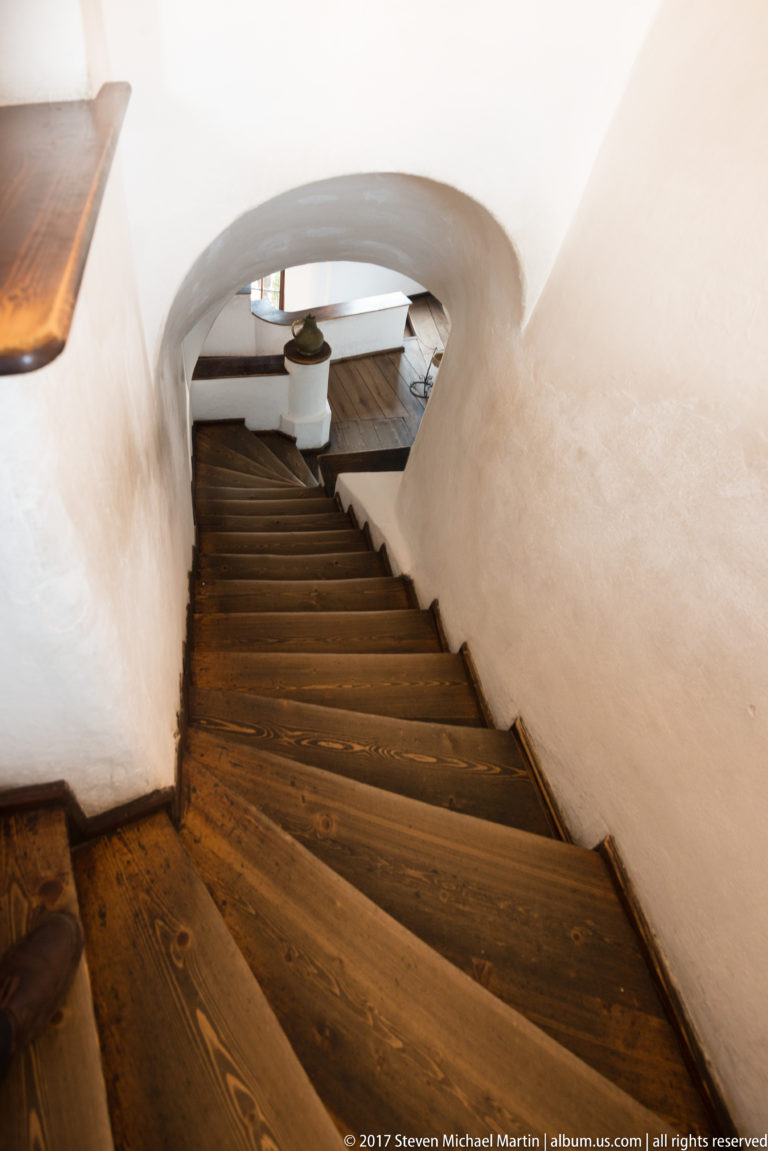 Steep wooden staircase descending through a narrow white-plastered passage inside Bran Castle.