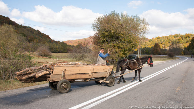 Horse-drawn wooden cart and two people traveling along a paved rural road near Bran.