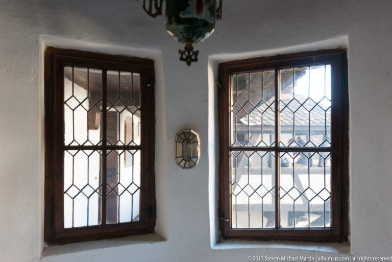 Two tall leaded-glass windows set into deep white-plastered wall recesses with dark wood frames.
