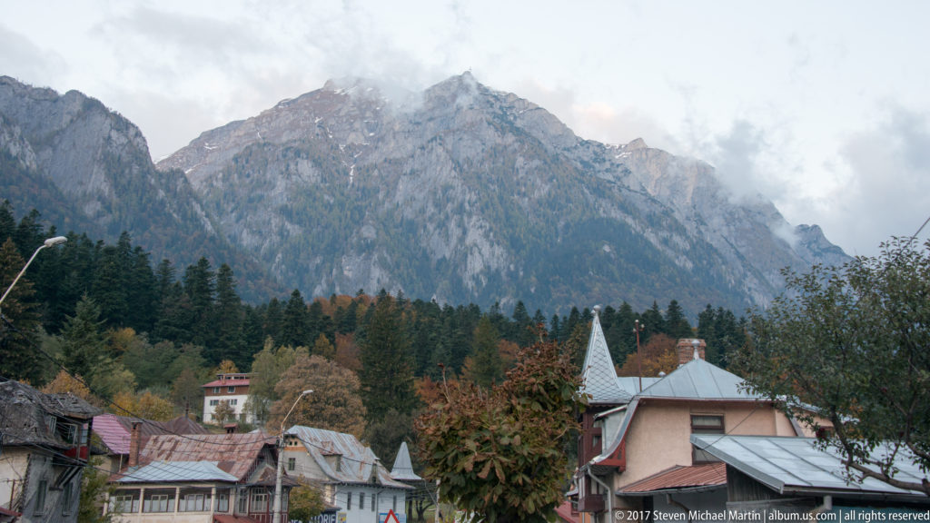 Rocky Carpathian peaks above conifer forest and clustered roofs near Brasov under low cloud.