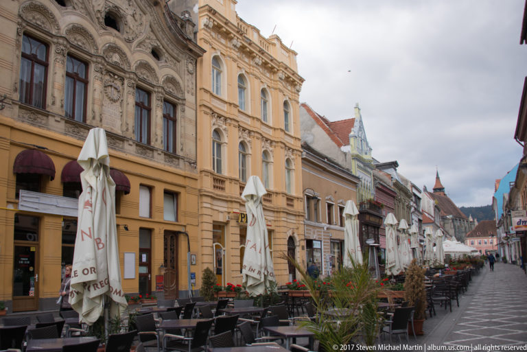 Ornate historic facades beside a long row of outdoor restaurant tables and folded umbrellas.