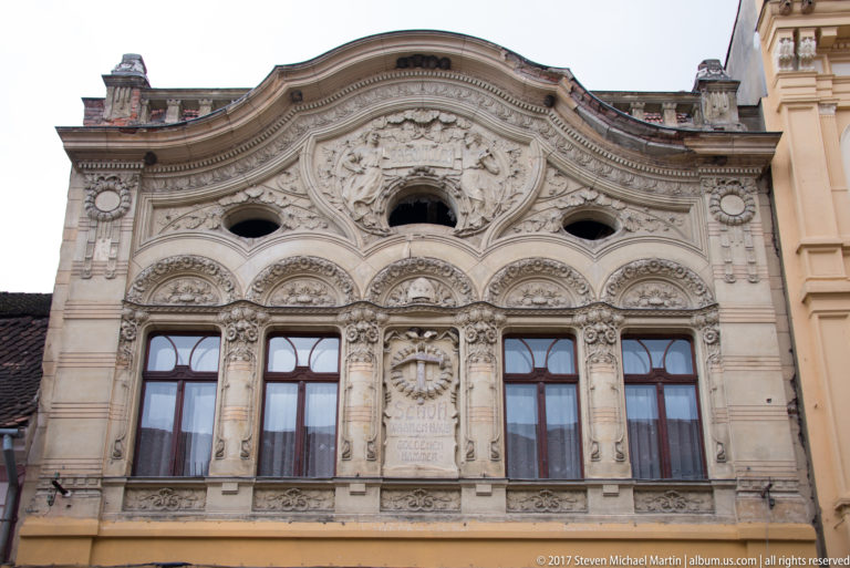 Pale historic facade with a curved gable, dense relief ornament, arched openings, and tall windows.