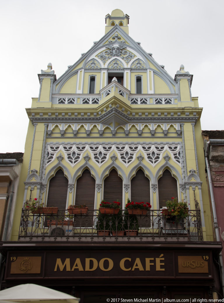 Yellow Mado Cafe facade with pointed arches, patterned trim, steep gable, and flower boxes.