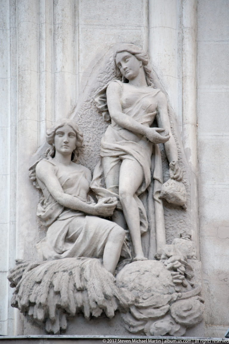 Pale stone relief with two female figures in flowing garments, one seated and one standing behind.