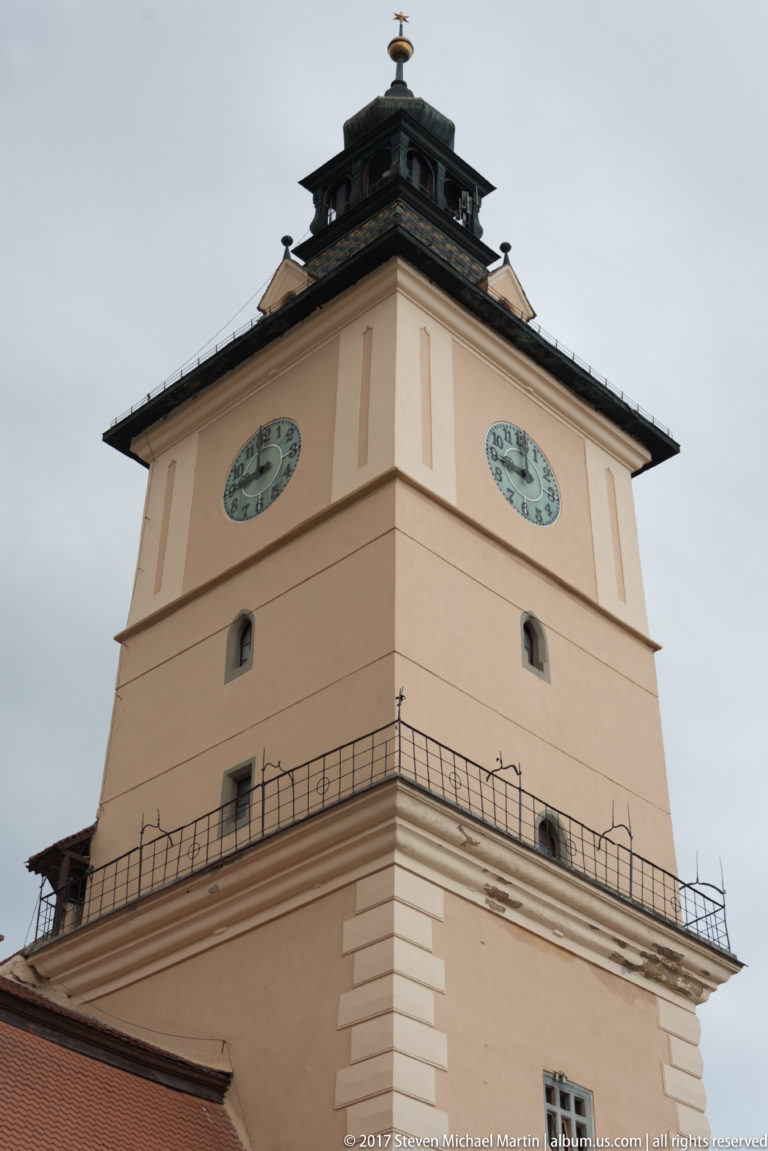 Close low-angle view of the Council House tower with two clock faces, gallery railing, and tiered roof.