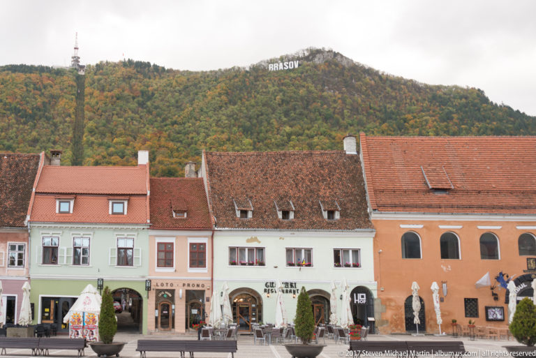 Pastel historic houses and cafes in Council Square with Tampa hill and the BRASOV sign above.