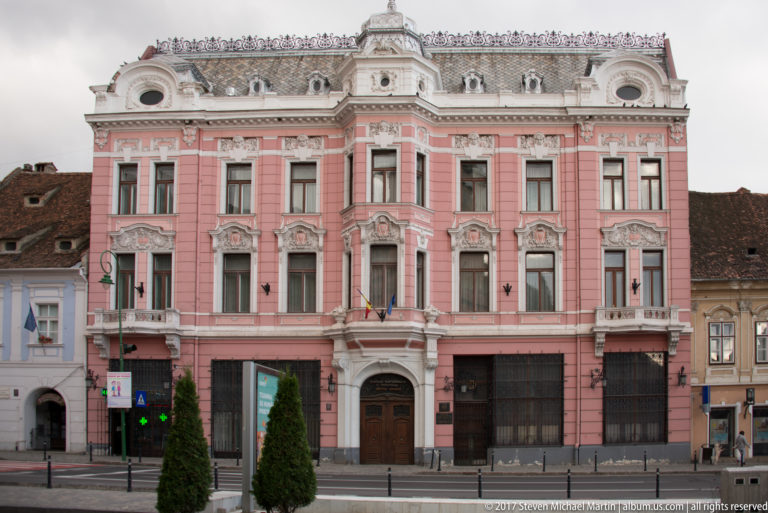 Ornate pink historic townhouse with carved window surrounds, projecting bay, flags, and decorative roofline.