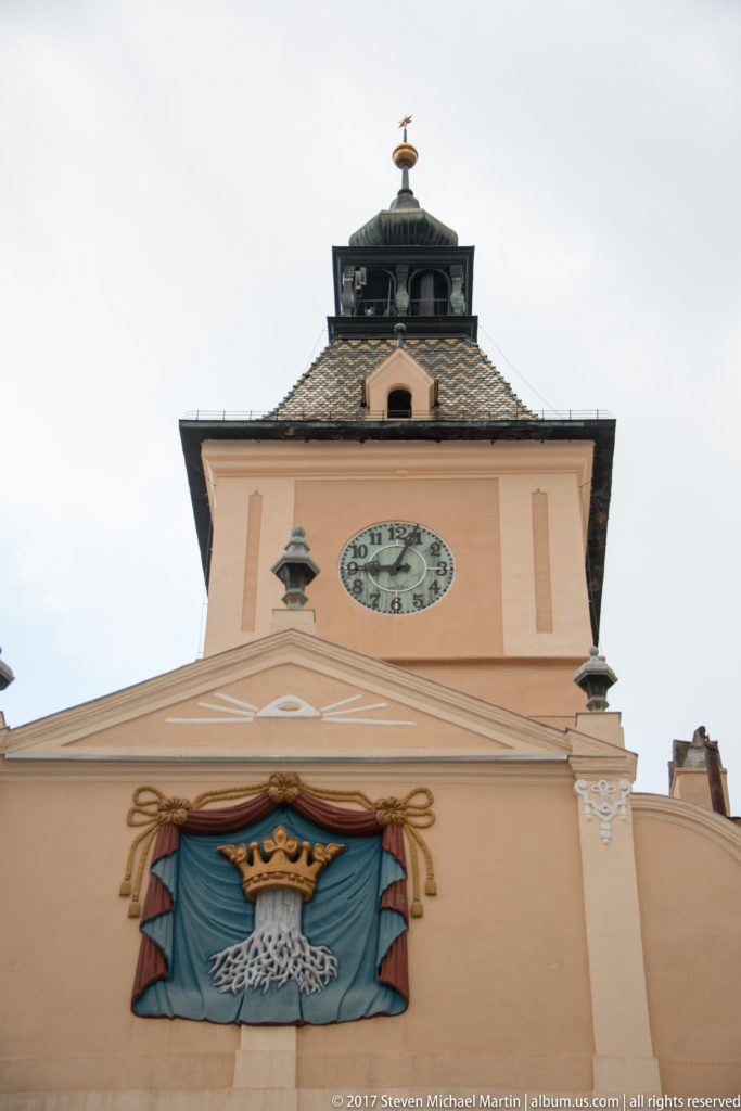 Council House clock tower above a large crowned-tree Brasov emblem set on blue drapery.