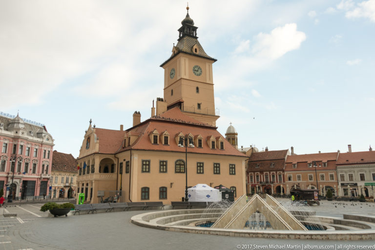 Council House clock tower behind the modern fountain and glass structures in Brasov Council Square.
