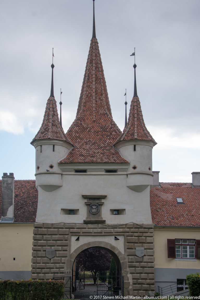 Catherine’s Gate in Brașov with a central steep roof, four corner turrets, and a large arched passage.