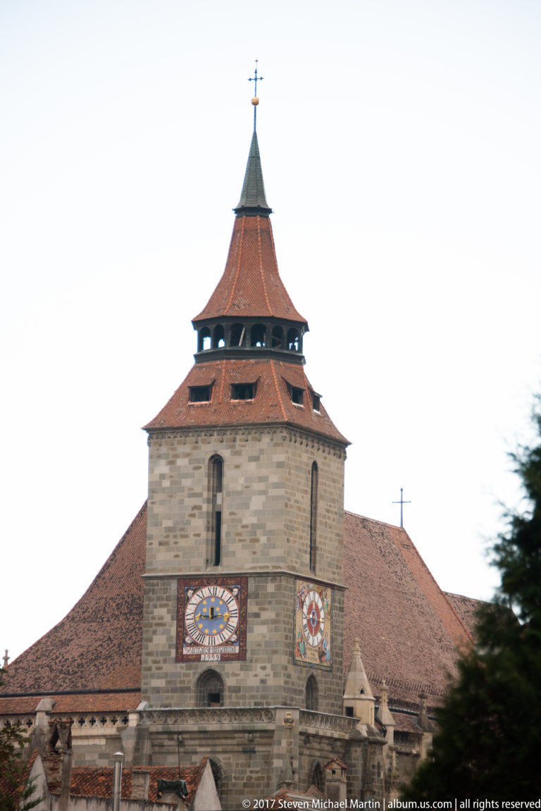 Stone tower of the Black Church with two painted clock faces beneath a red-tiled roof and belfry.