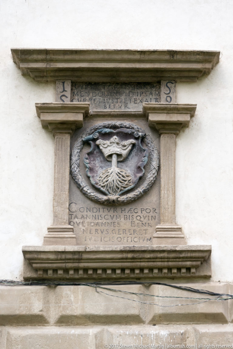 Stone heraldic plaque with a crowned bird emblem in an oval medallion above a Latin inscription.