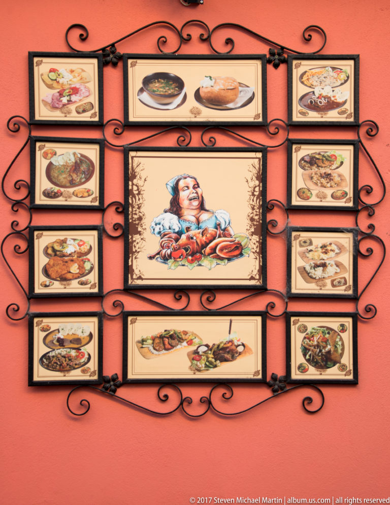 Framed restaurant food photographs arranged around a central folk-style illustration on a red wall.