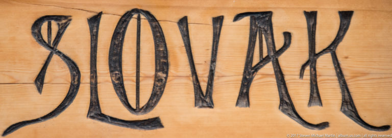 Black hand-painted word “SLOVAK” in elongated decorative lettering on a wooden sign.