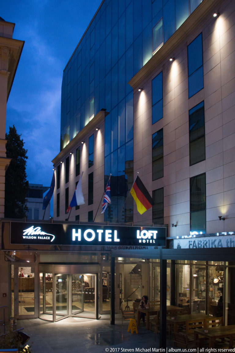 Blue-hour exterior of Loft Hotel Bratislava with illuminated HOTEL and LOFT signage above a glass-fronted entrance.