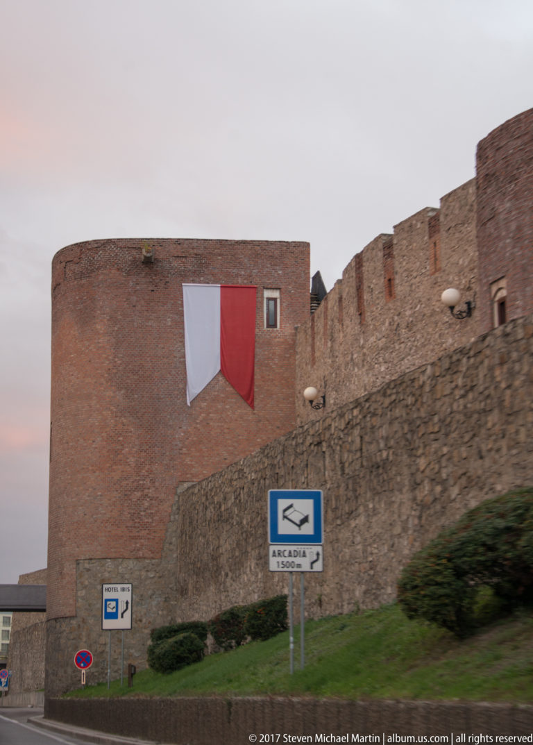Brick and stone fortification walls beside a roadway below Bratislava Castle, with a large red-and-white banner on the masonry.