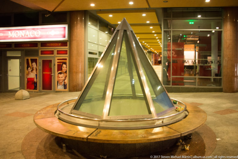 Conical glass skylight with metal ribs set in a circular base inside a brightly lit Bratislava shopping passage.