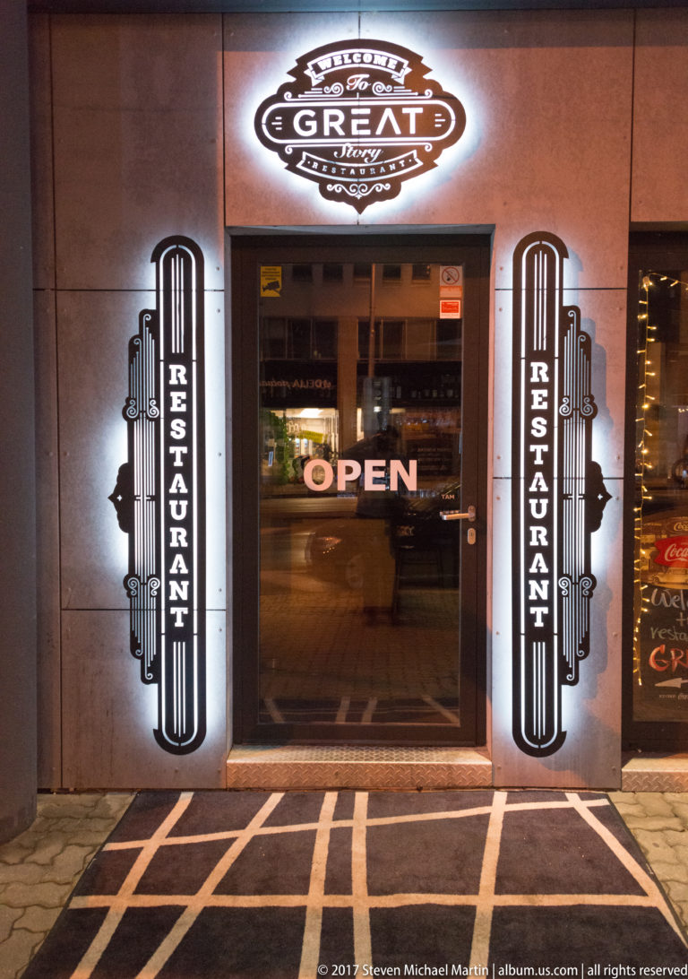 Nighttime restaurant entrance with glowing GREAT sign, vertical RESTAURANT panels, and an OPEN sign in the doorway.