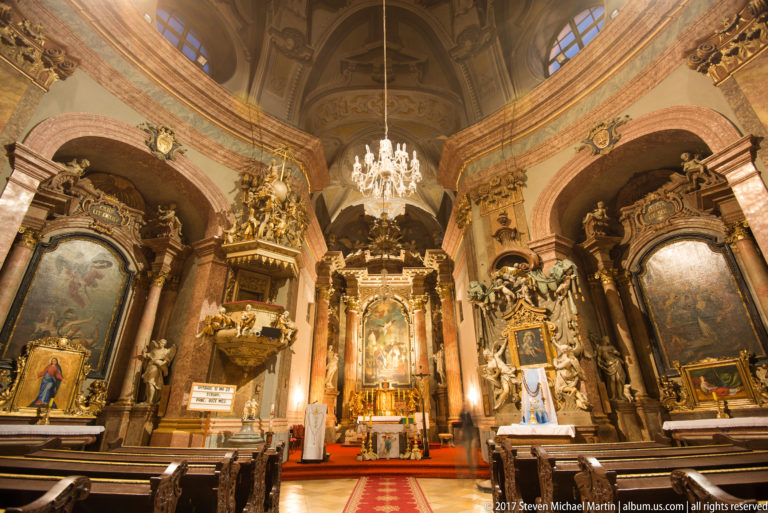 Baroque interior of the Trinitarian Church with gilded side altars, central sanctuary, painted vaults, and chandelier.