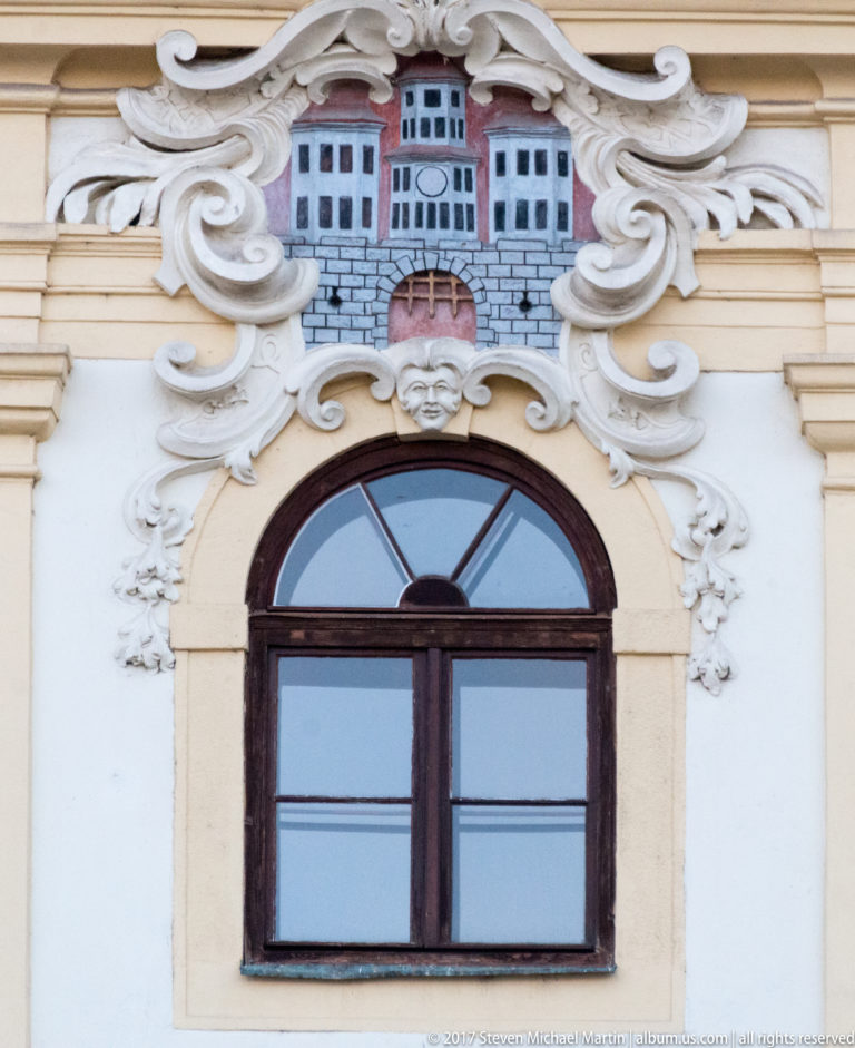 Relief of Bratislava’s city coat of arms framed by white stucco scrolls above an arched window.