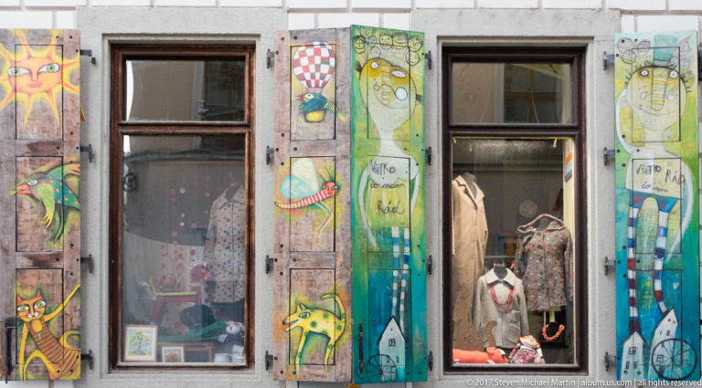 Shop windows framed by brightly painted wooden shutters decorated with stylized faces and animals in Bratislava.