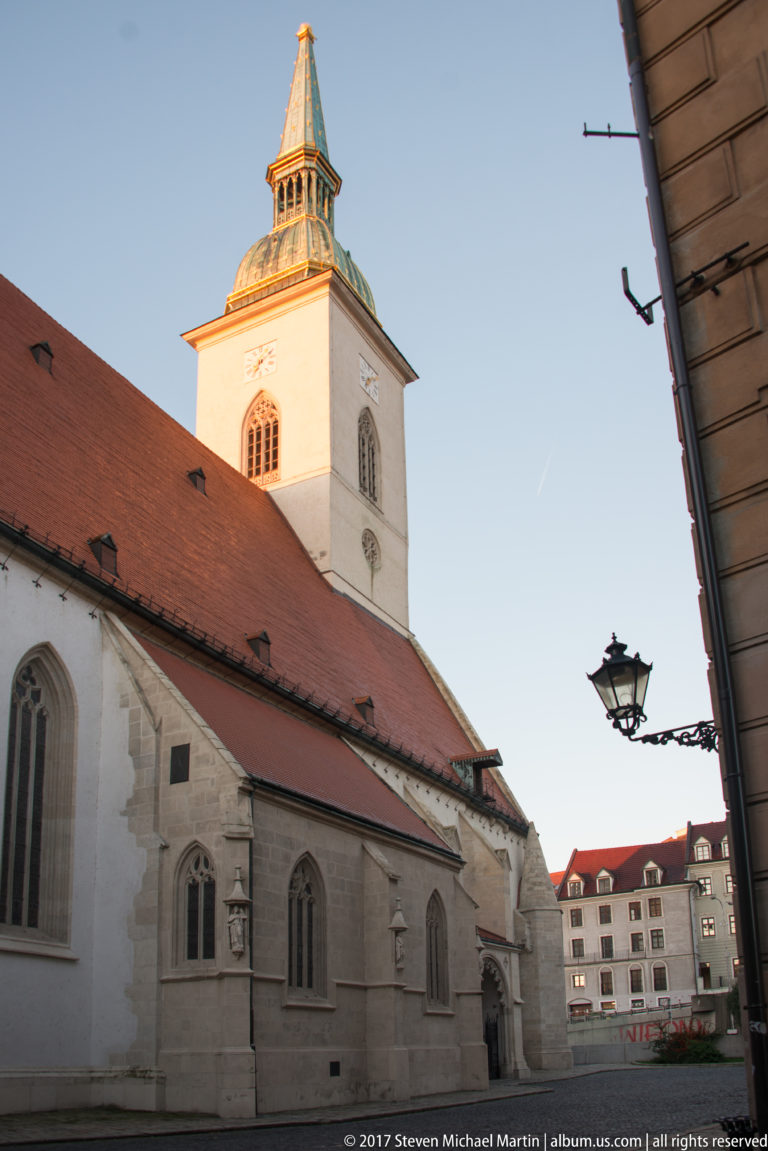 Historic Gothic church with pale stone walls, red tiled roof, pointed windows, and square white tower.