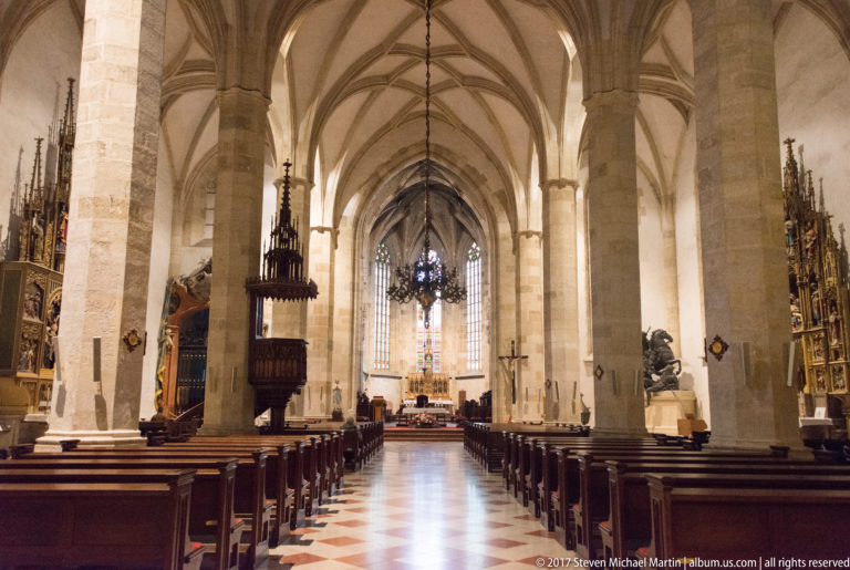 Gothic church nave with stone piers, ribbed vaults, carved pulpit, side altarpieces, and distant sanctuary.