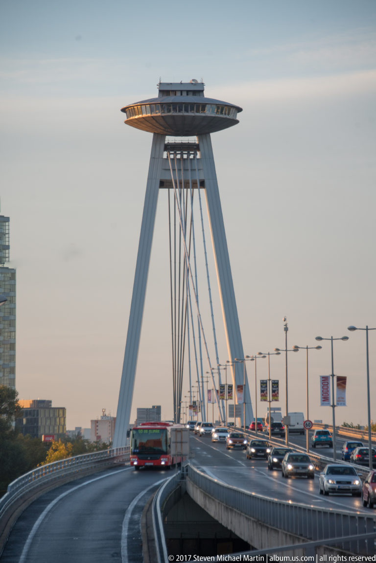Cars and bus approaching the Most SNP beneath its inclined pylon and saucer-shaped observation deck.