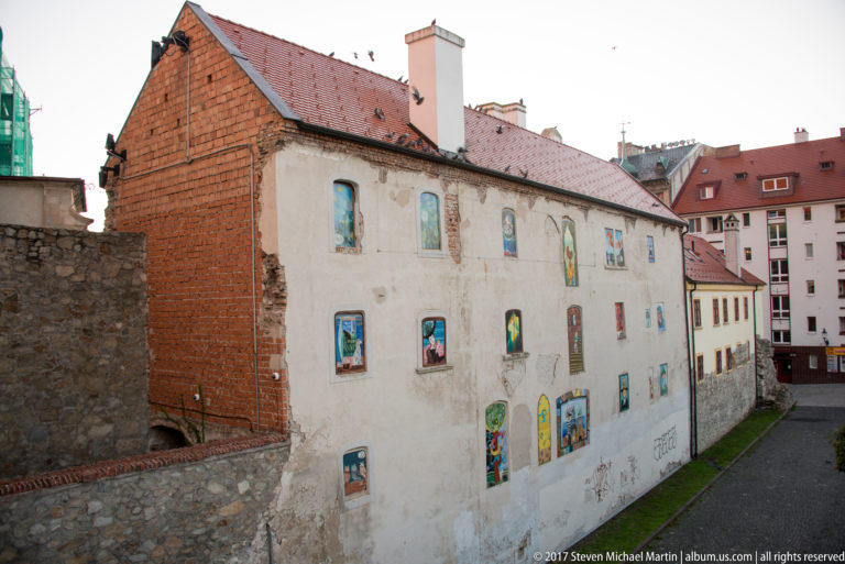 Weathered historic building with exposed brick and colorful painted panels filling multiple window openings.