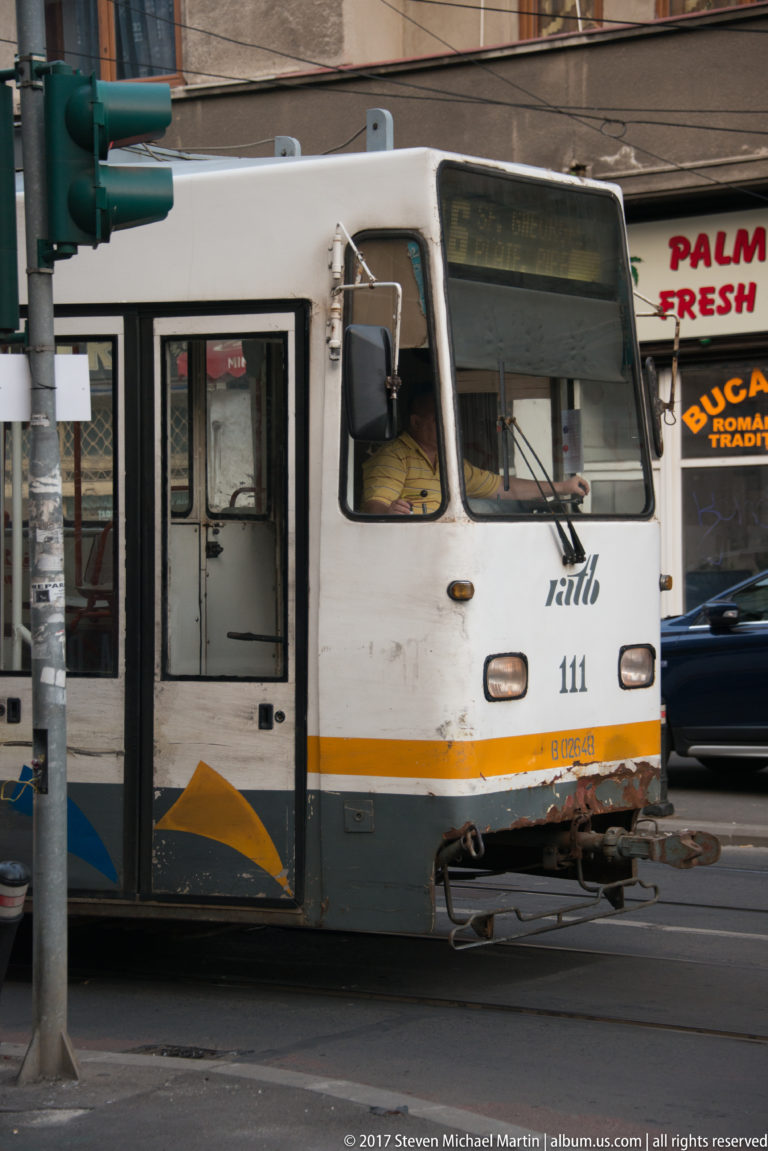Close view of an older white Bucharest tram showing windshield, doors, fleet number, coupler, and yellow-blue trim.