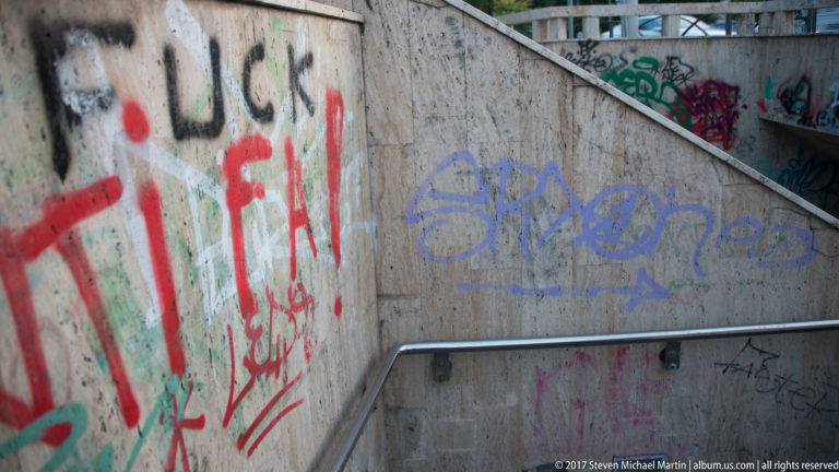 Concrete Bucharest stairwell with metal handrail and retaining walls densely covered in colorful graffiti and spray-painted tags.