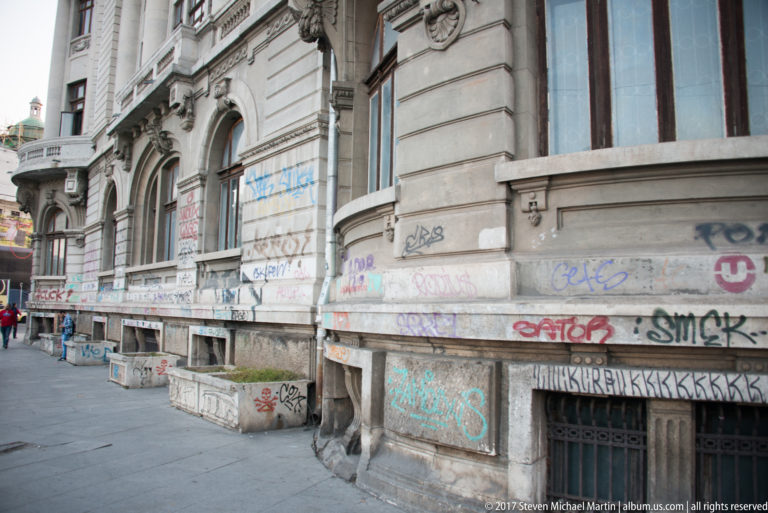 Ornate historic Bucharest building with curved bays and rusticated stone base heavily covered in colorful graffiti and tags.