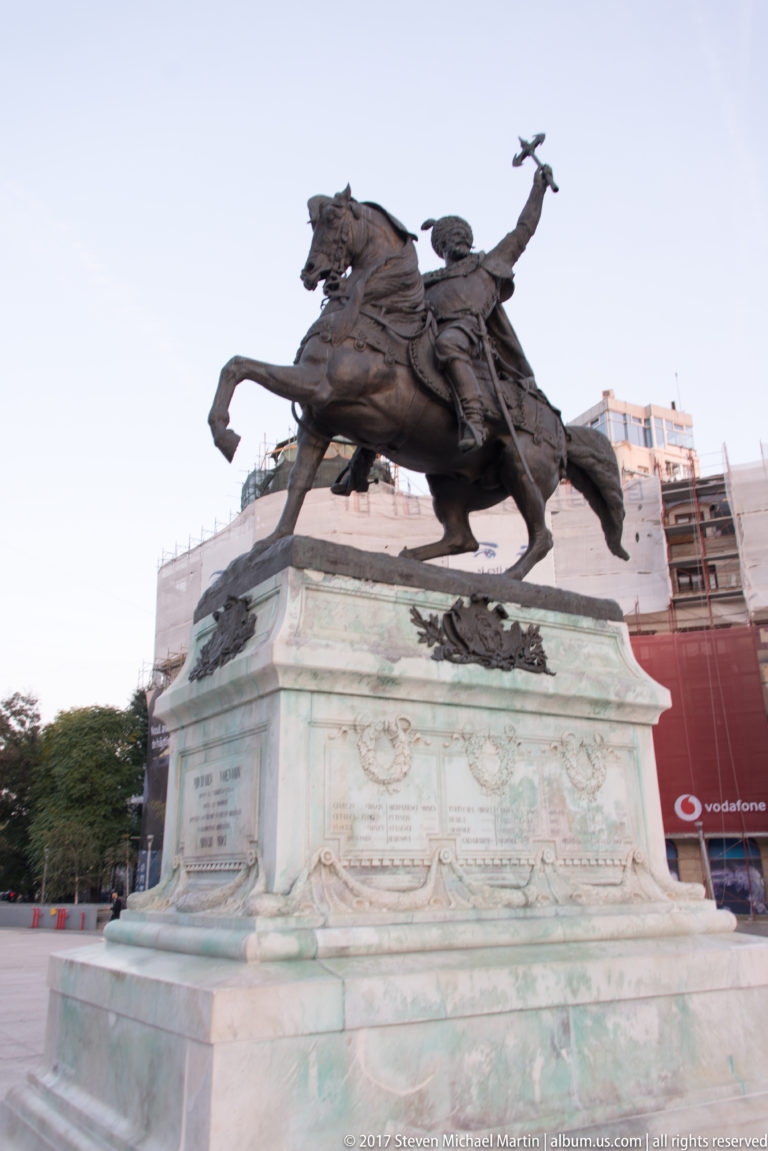 Bronze equestrian statue of Michael the Brave on a large decorated stone pedestal in Bucharest University Square.