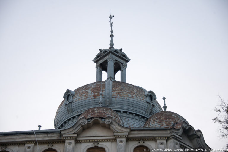 Ornate Bucharest roofline with broad metal-clad dome, open lantern, finial, scroll ornaments, and smaller adjacent dome.