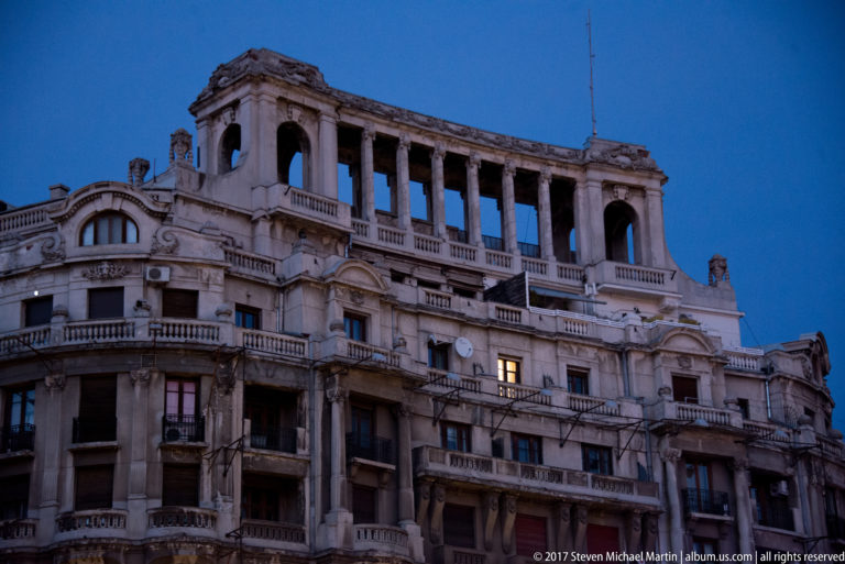 Ornate historic Bucharest building with balconies, pilasters, sculpted stonework, and a tall open-arched loggia at the roofline.