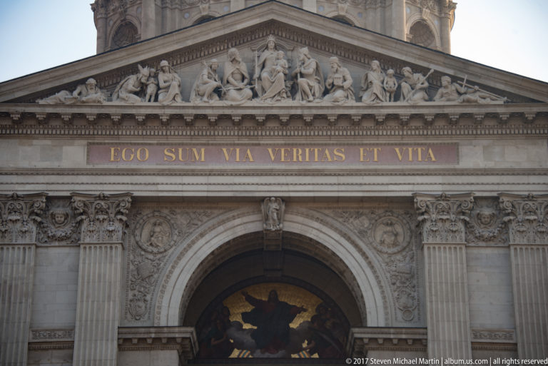 St. Stephen’s Basilica entrance with sculpted pediment, Corinthian columns, Latin inscription, and Christ mosaic.