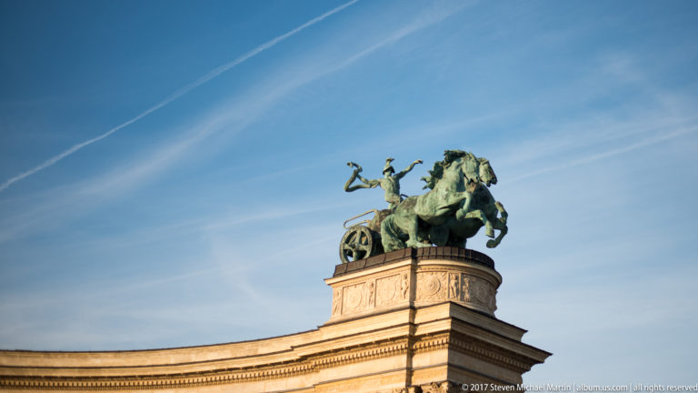 Bronze chariot group with horses and upright figure on a stone pavilion at Heroes’ Square.