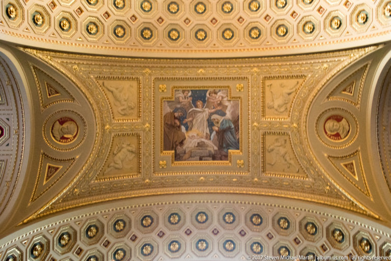 Figurative ceiling painting framed by gilded borders, circular medallions, relief panels, and decorative coffers.