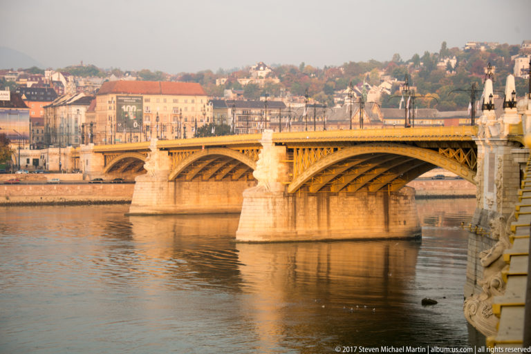 Margaret Bridge spanning the Danube with repeating iron arches, stone piers, and Buda buildings beyond.
