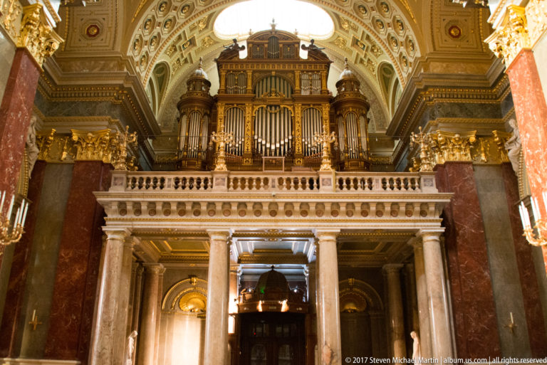 Large pipe organ above a columned gallery amid red marble and gilded decoration in St. Stephen’s Basilica.