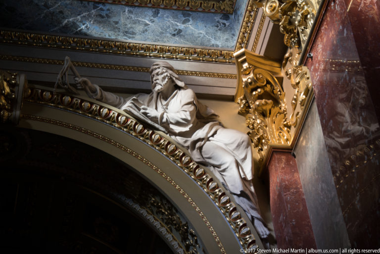 White reclining sculpted figure above an ornate arch with gilding, colored marble, and blue decorative panels.