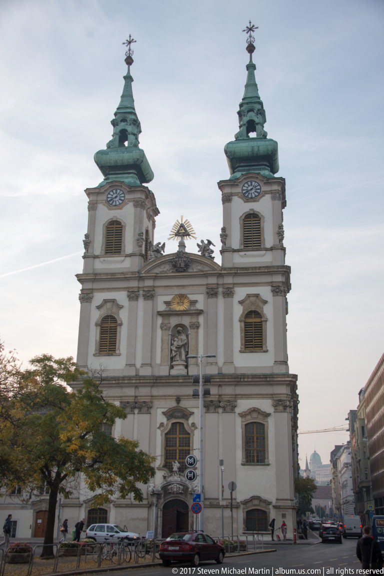 Frontal view of Saint Anne Church with twin green towers, pale Baroque façade, arched windows, and statuary niches.
