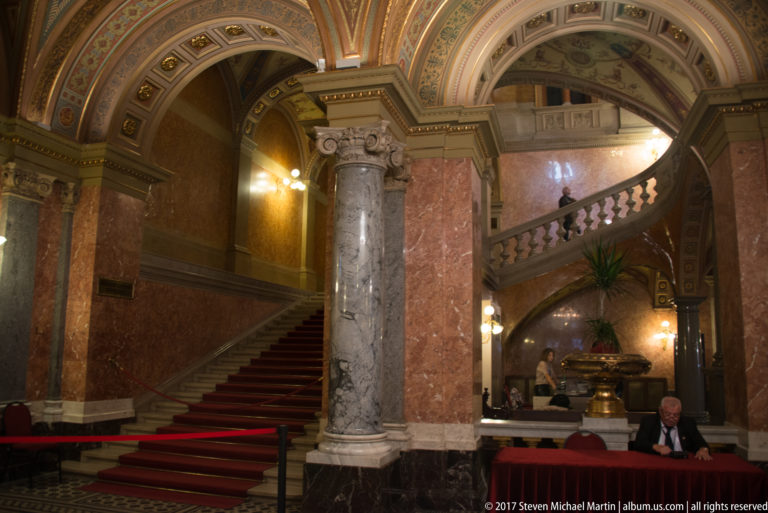 Red-carpeted marble staircase with columns, balustrades, painted vaults, and gilded decoration inside the opera house.